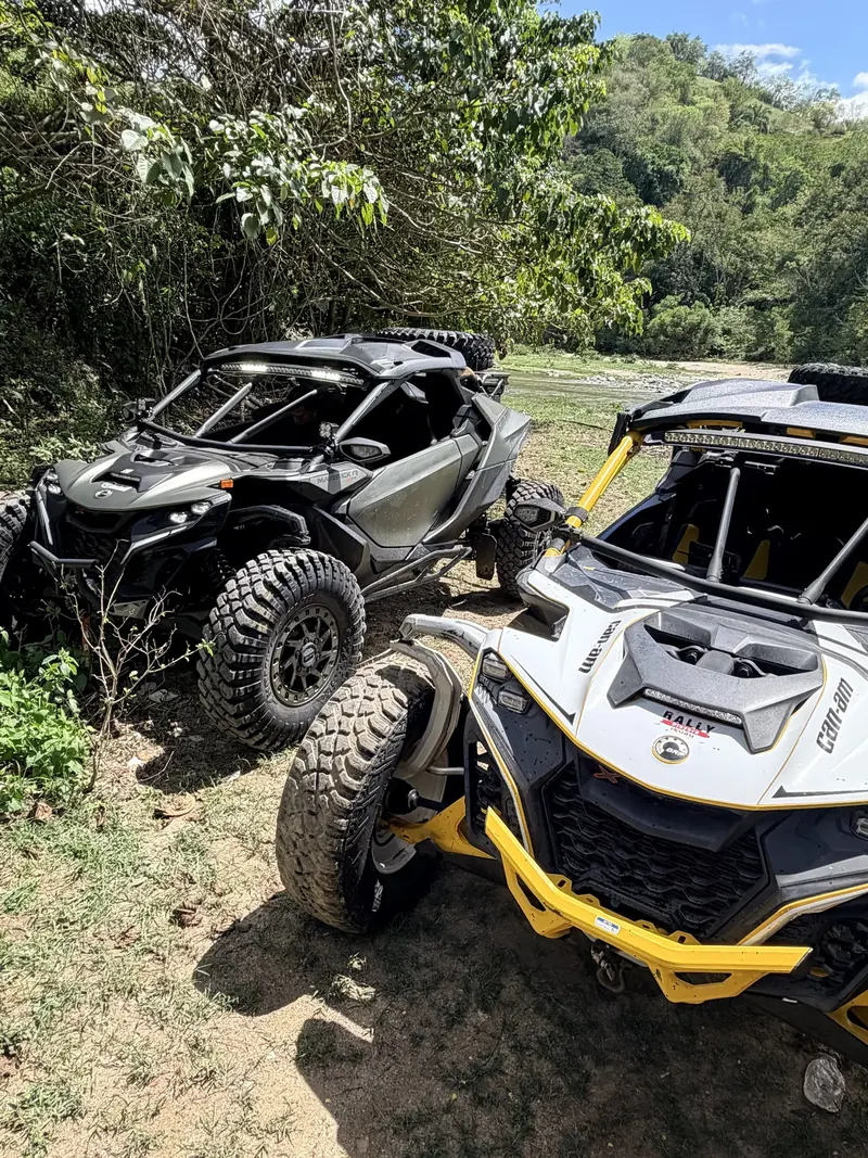 Black Can-Am Maverick R and a white and yellow Can-Am parked by a river